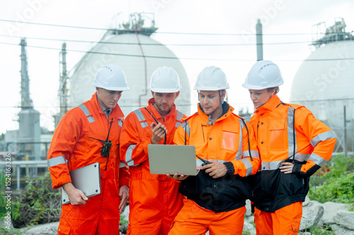 Group of gas factory technicians or  engineers with one hold laptop and discuss together about their work and stay in front of tank with day light.