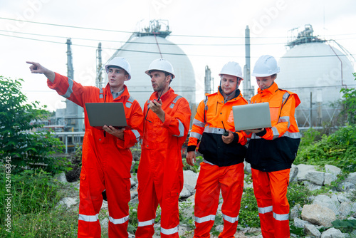 Group of gas factory technicians or  engineers with one hold laptop and other one point to his right side and discuss together about their work and stay in front of tank with day light.