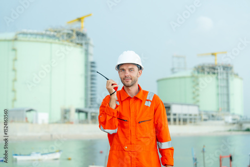 Petrochemical or gas factory worker talk with walkie talkie and look at camera and stand in front of tank in factory.