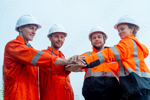 Lower view of group of petrochemical workers or technicians stand and hold hands together in front of factory tank.