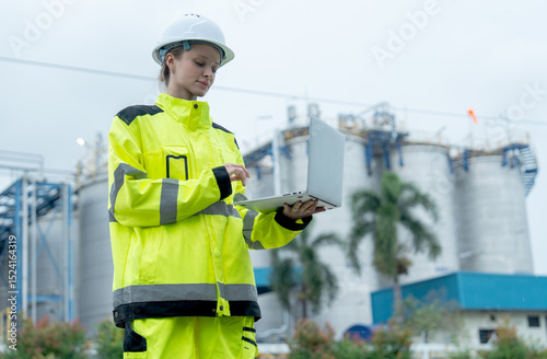 One petrochemical or gas factory worker woman hold laptop for working with smiling in front of the factory.