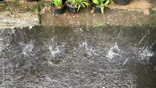 Heavy raindrops hitting a wet, uneven concrete or asphalt surface create lots of splashes and ripples in small puddles.