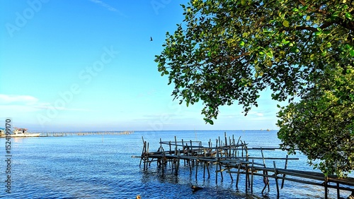 Scenic view of calm blue sea with bamboo bridge under shady tree at Alar Beach, Tangerang, Indonesia