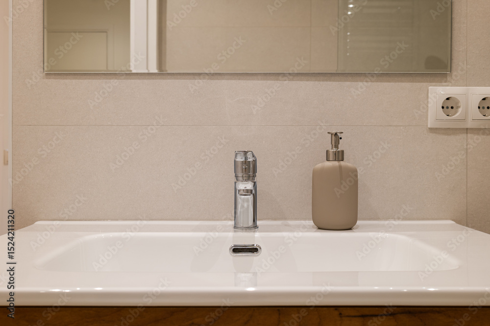 Front view of a modern bathroom sink with chrome faucet and beige soap dispenser below a large mirror Front view of a modern bathroom sink with chrome faucet and beige soap dispenser below a large mirror