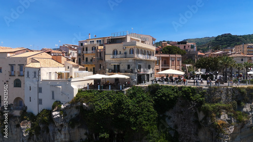 People relaxing at cafe tables overlooking scenic coastline in Tropea, Italy