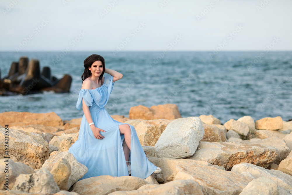 Beautiful young girl with long dark hair in a blue long dress on the beach at sea in summer Beautiful young girl with long dark hair in a blue long dress on the beach at sea in summer