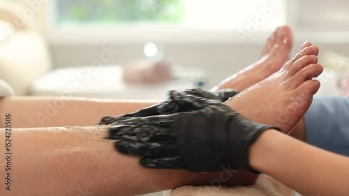 Asian nail salon worker wearing black gloves perform foot scrub treatment at spa. Focus on hands and feet, showcasing exfoliation process. small business, beauty care and gentleness.