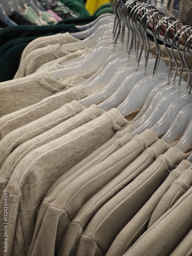 Fototapeta premium Beige sweatshirts neatly arranged on hangers in a clothing store during daylight hours