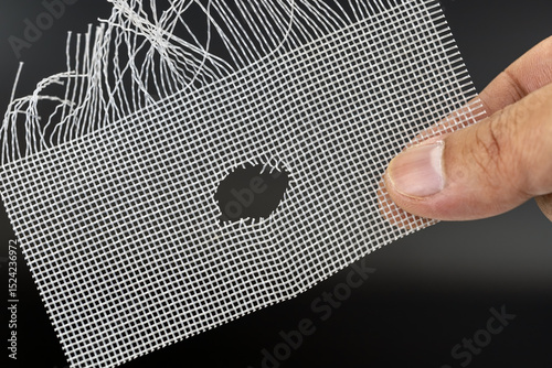 Hand holds damaged wire mesh with hole, possibly caused by rat. mesh is frayed and shows signs of wear, highlighting need for repair or replacement