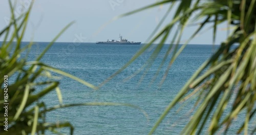 view through palm trees on a warship of the Thai Armed Forces stands in sea at sunny day
