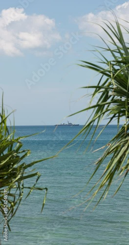 view through palm trees on a warship of the Thai Armed Forces stands in sea at sunny day