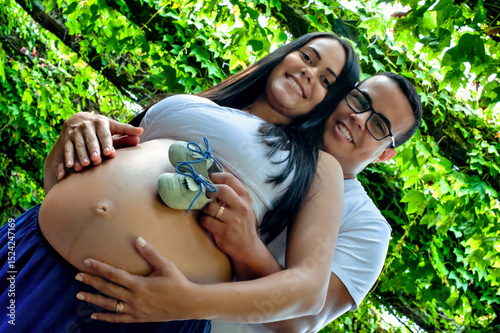 Happy Expecting Couple with Baby Shoes on Pregnant Belly