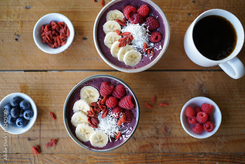 Wallpaper Mural Two vibrant purple smoothie bowls, adorned with raspberries, banana slices, goji berries, and coconut flakes, sit on a rustic wooden table next to a cup of coffee Torontodigital.ca