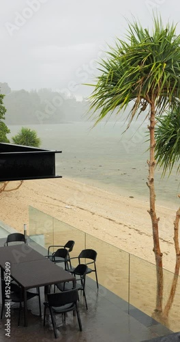 luxury villa with pool during heavy rain, balconies, palm trees on the beach, nobody, view from terrace on the beach, blue sea and islands in the background