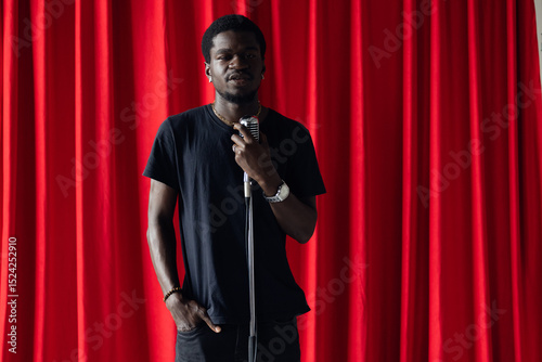 Bilde på lerret Happy young african american man comic tells stand up monologue on stage with red curtains