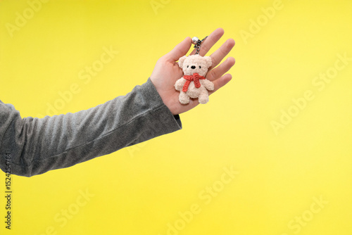 hand holding cute bear keychain in yellow background