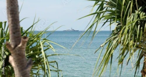 view through palm trees on a warship of the Thai Armed Forces stands in sea at sunny day