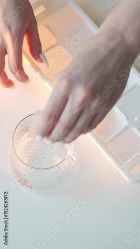 Woman’s hands take an ice cube, put it in a glass and pour water – 4K, warm lighting