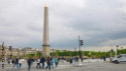 People walk along the pedestrian crossing over Place de la Concorde with views of the Obelisque de Louxor and the Jardin des Tuileries on a cloudy spring day in 1st arrondissement. Out of focus. Paris