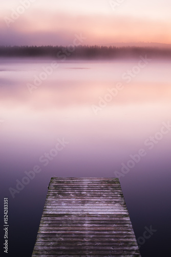 Misty sunrise over a tranquil jetty on a lake in Sweden captures serene morning beauty