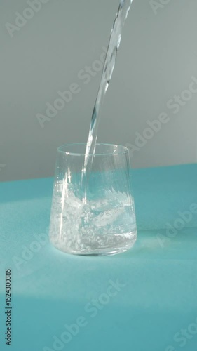 Clean water pouring into a glass with ice cube, slow motion, 4K