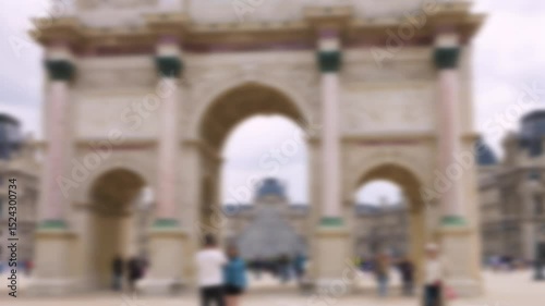 People stroll along the Place du Carrousel  and take pictures in front of the Arc de Triomphe du Carrousel on a clear sunny spring day. Out of focus. Paris, France.