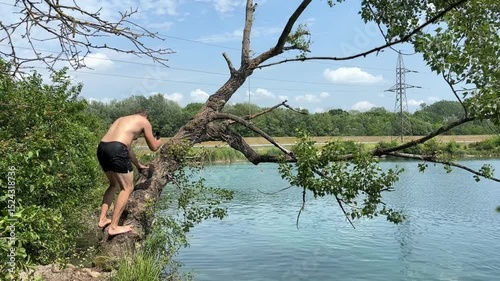 Man climbing a tree above a body of water, preparing to jump in, capturing a daring and adventurous summer activity.