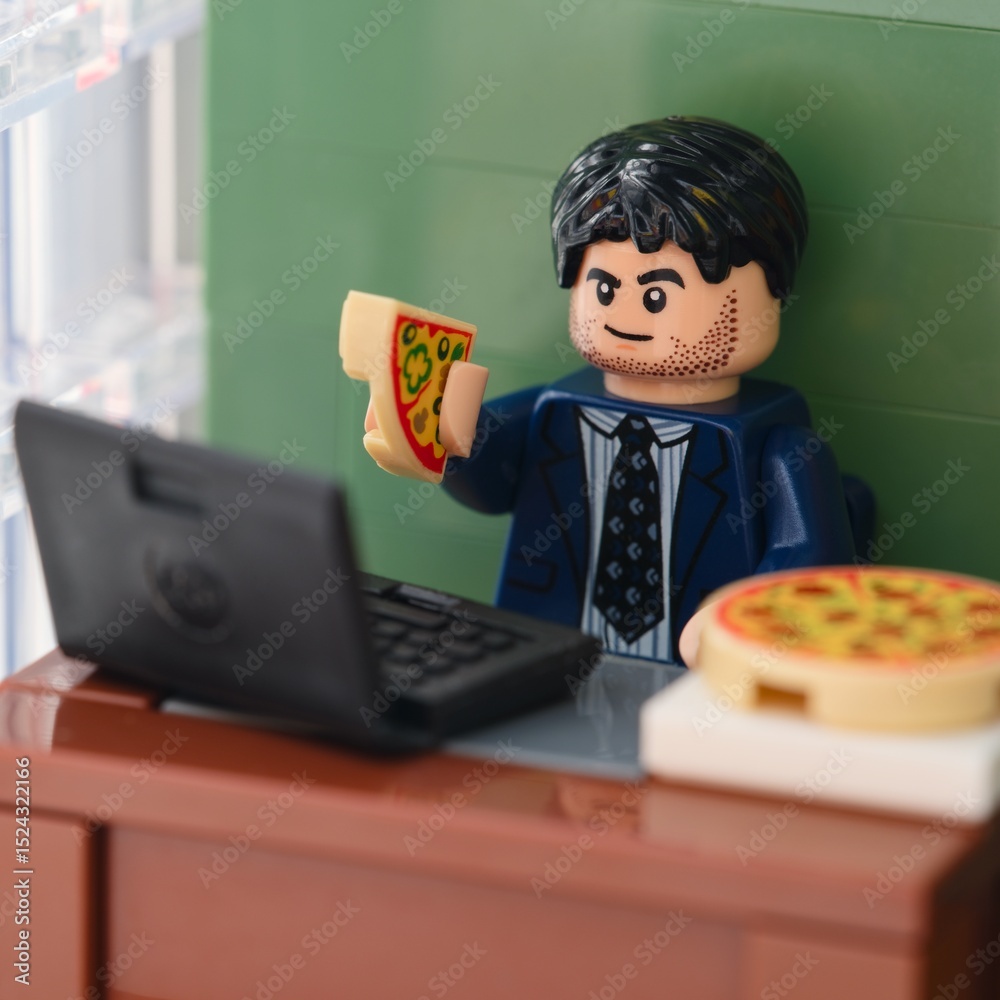 Obraz premium Tambov, Russian Federation - February 17, 2025 Lego businessman sitting behind a table with a laptop on it in an office and eating pizza. Close-up