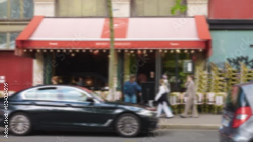 View of cars driving along Quai de la Megisserie, people walking along the street and relaxing at the Coquelicot bistro. Out of focus. Paris, France.