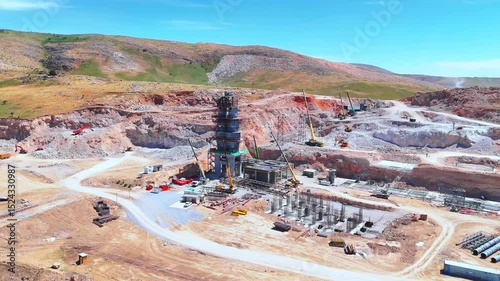 Industrial construction site with tower and machinery in hills, aerial daytime view.