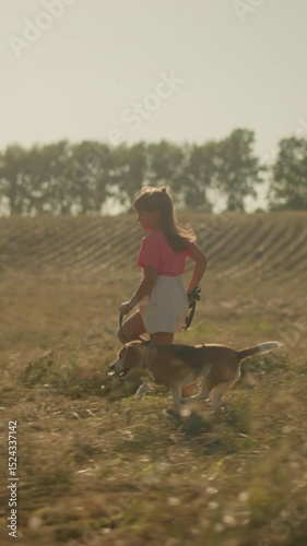 Young girl runs joyfully with her dog on a leash through open farmland, capturing carefree childhood, strong bond with pet, and love for outdoor adventure