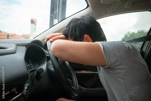 Asian man slumping over steering wheel in exhaustion, bad traffic
