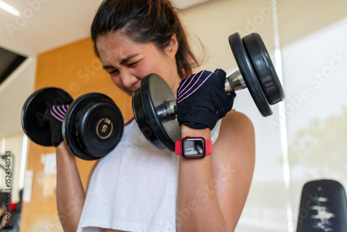 Asian female focusing and showing intense effort during heavy dumbbell curls