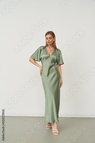 Elegant woman in stylish green dress poses gracefully in a modern studio setting