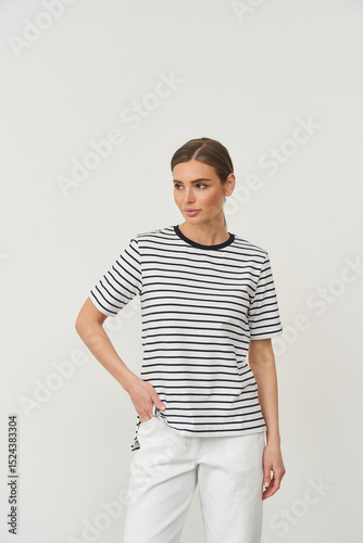 Woman in a short-sleeved black and white striped shirt with a round neck. She has light brown hair tied back and wears white pants. She's standing with her hand on her hip