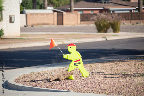 Plastic figure in fluorescent yellow holding an orange flag and signed to encourage drivers to slow down