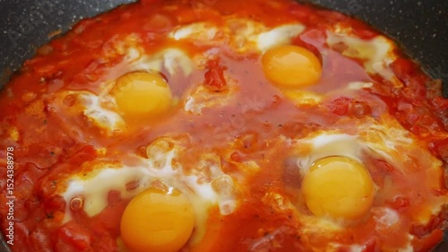 Simmering shakshuka with eggs, peppers, onions in tomato sauce, traditional Middle Eastern dish, healthy meal, cooking process.