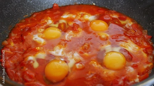 Shakshuka simmering in a pan on the stove: tomato sauce with vegetables and eggs. A traditional Middle Eastern dish, healthy and delicious breakfast.