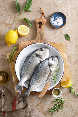 Fresh raw sea bream fish or dorado fish with lemon and herbs, top view
