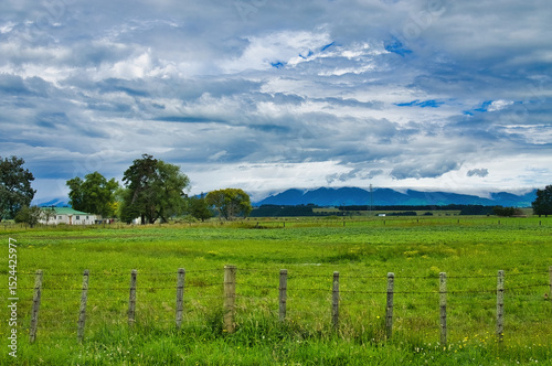 Green meadows, old fence, simple farmhouse and dark hills under a dramatic sky. Manawatu region, North Island, New Zealand, close to Fielding.
