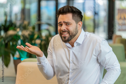 What. Why. Angry Caucasian businessman raising hands in indignant expression, asking reason of failure, demonstrating disbelief irritation by troubles. Young bearded guy sitting in modern office lobby