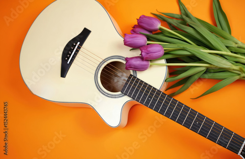 White acoustic guitar with purple tulips on orange background. Springtime theme, music concept. Relaxation, rest, melody, sound, stringed instrument, musical instrument for music lovers.