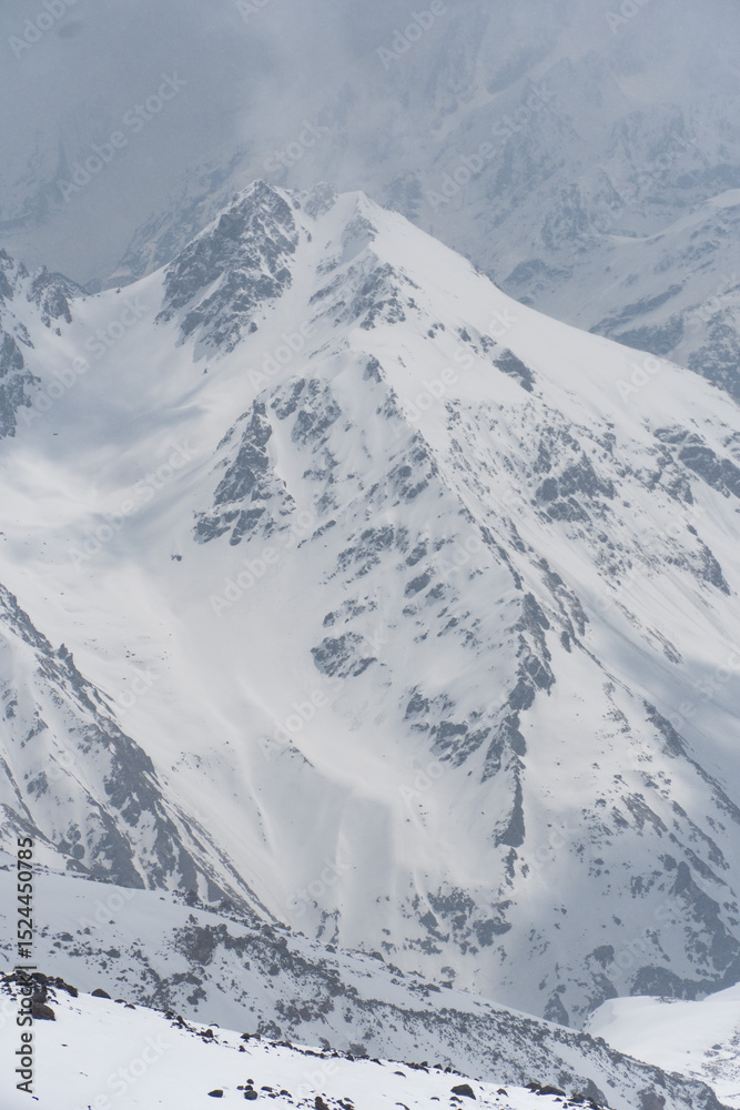 Obraz premium Snow-covered mountain peaks of Mount Elbrus, Kabardino-Balkaria, Russia, captured under dramatic cloudy skies