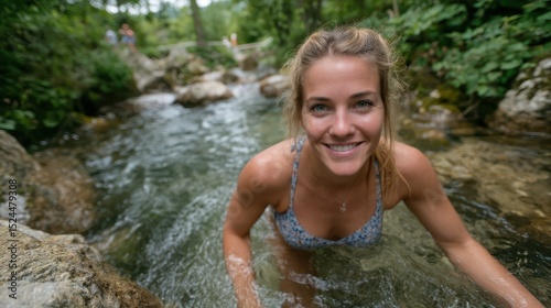 A joyful woman swims in a tranquil stream, embracing the refreshing waters of nature, highlighting the essence of outdoor fun and the beauty of the natural environment.