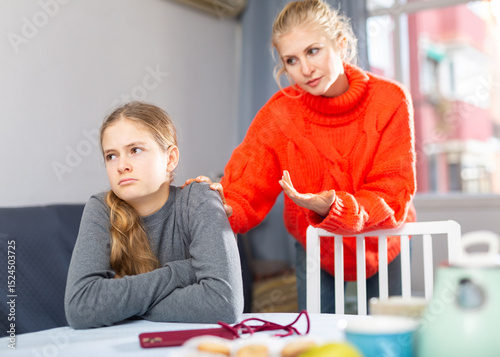 Upset teenager girl after quarrel with her mother in domestic interior, mother consoles daughter