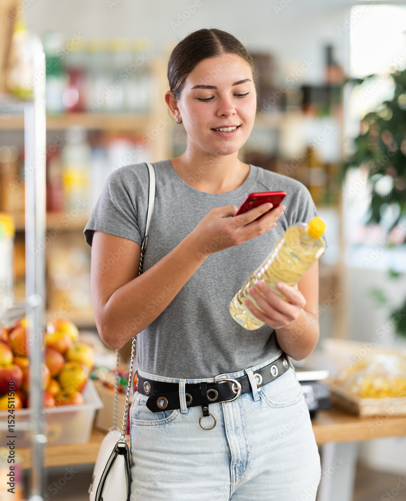 Φωτογραφία Smiling woman scanning a bottle of vegetable oil through an online app on mobile phone