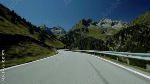 Breathtaking mountain road winding through lush greenery and rocky peaks under a clear blue sky.