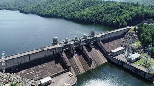 Aerial view of a massive concrete dam surrounded by lush greenery and calm water.