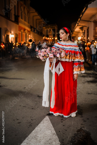 Mujer sahumadora vestida con traje típico tradicional participa en una procesión nocturna durante la Semana Santa en Popayán, Colombia. Sostiene un ramo de flores mientras esparce sahumerio 