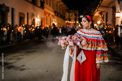 Mujer sahumadora vestida con traje típico tradicional participa en una procesión nocturna durante la Semana Santa en Popayán, Colombia. Sostiene un ramo de flores mientras esparce sahumerio 